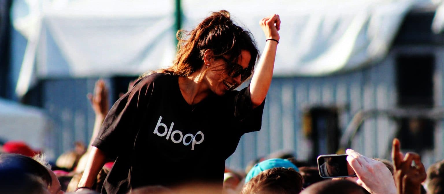 Il pubblico di un festival visto da dietro, con una ragazza in maglietta Bloop che balla sulle spalle