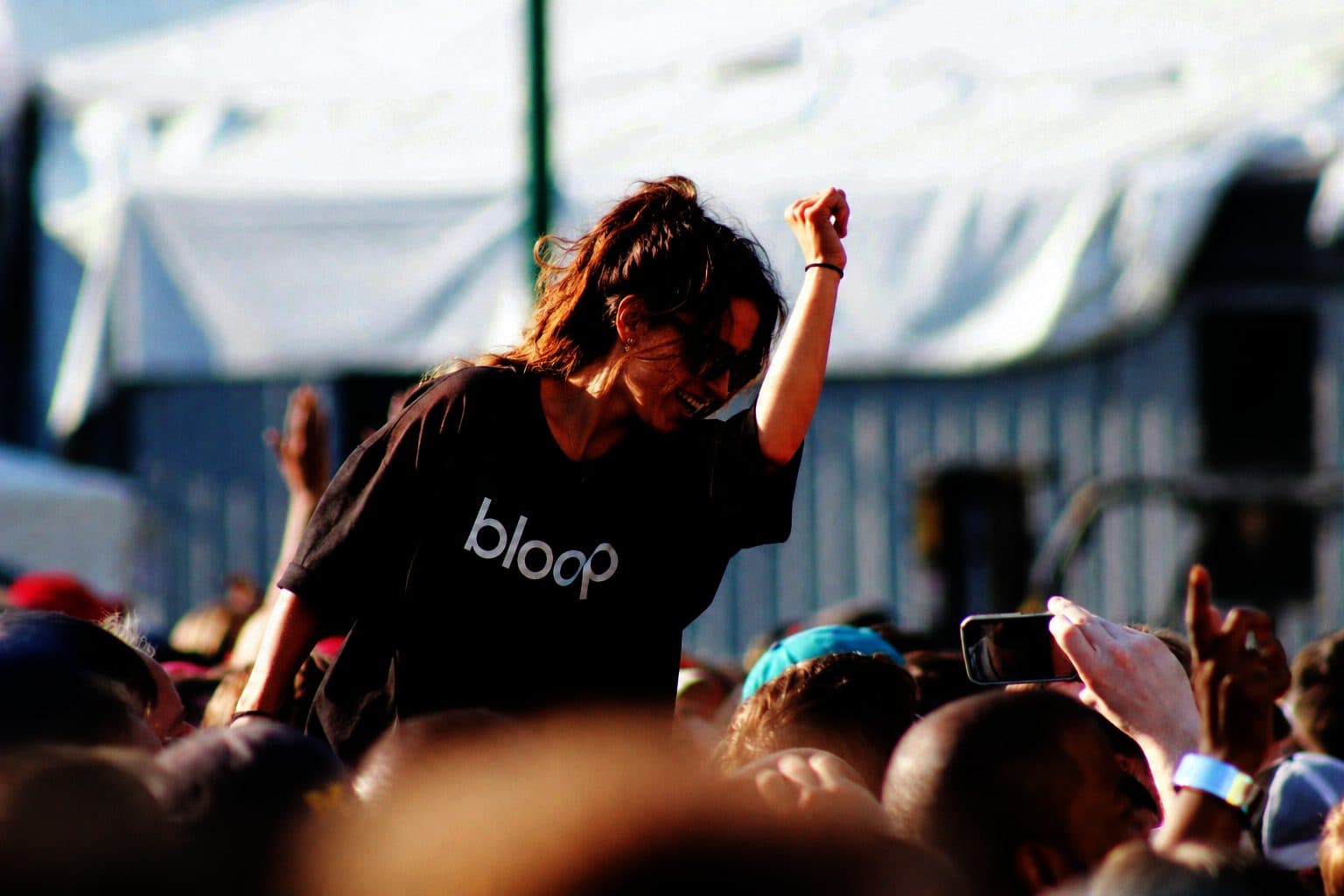 Una ragazza in maglietta Bloop sulle spalle di qualcuno, in mezzo al pubblico di un festival