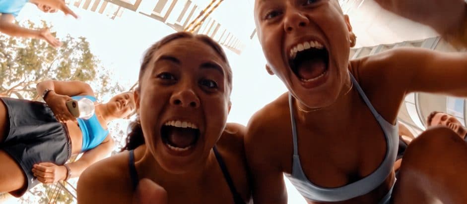 Due ragazze che urlano di gioia verso l'obiettivo, riprese dal basso in mezzo a un gruppo